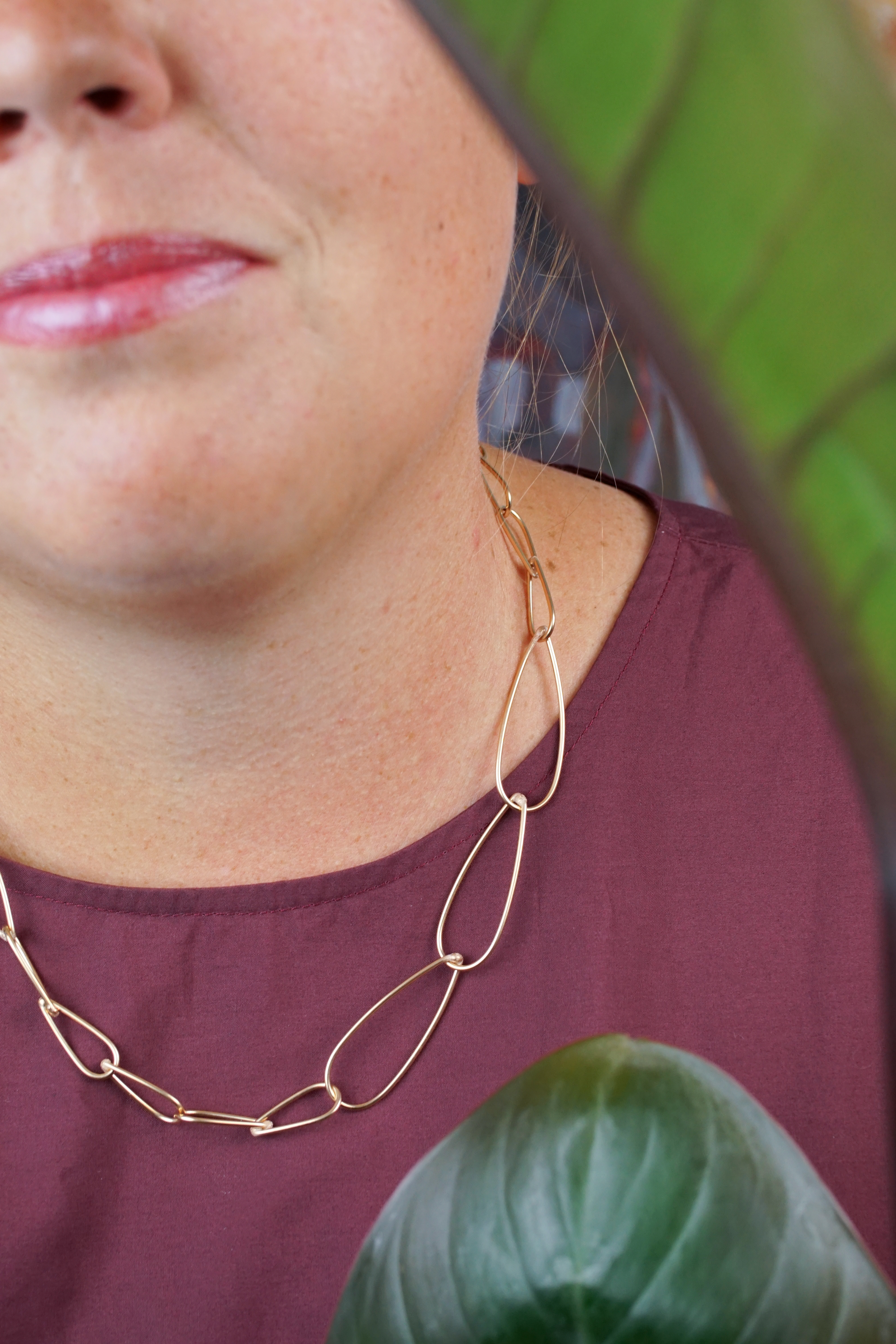 handcrafted bronze chain necklace, burgundy dress, and philodendron rojo congo