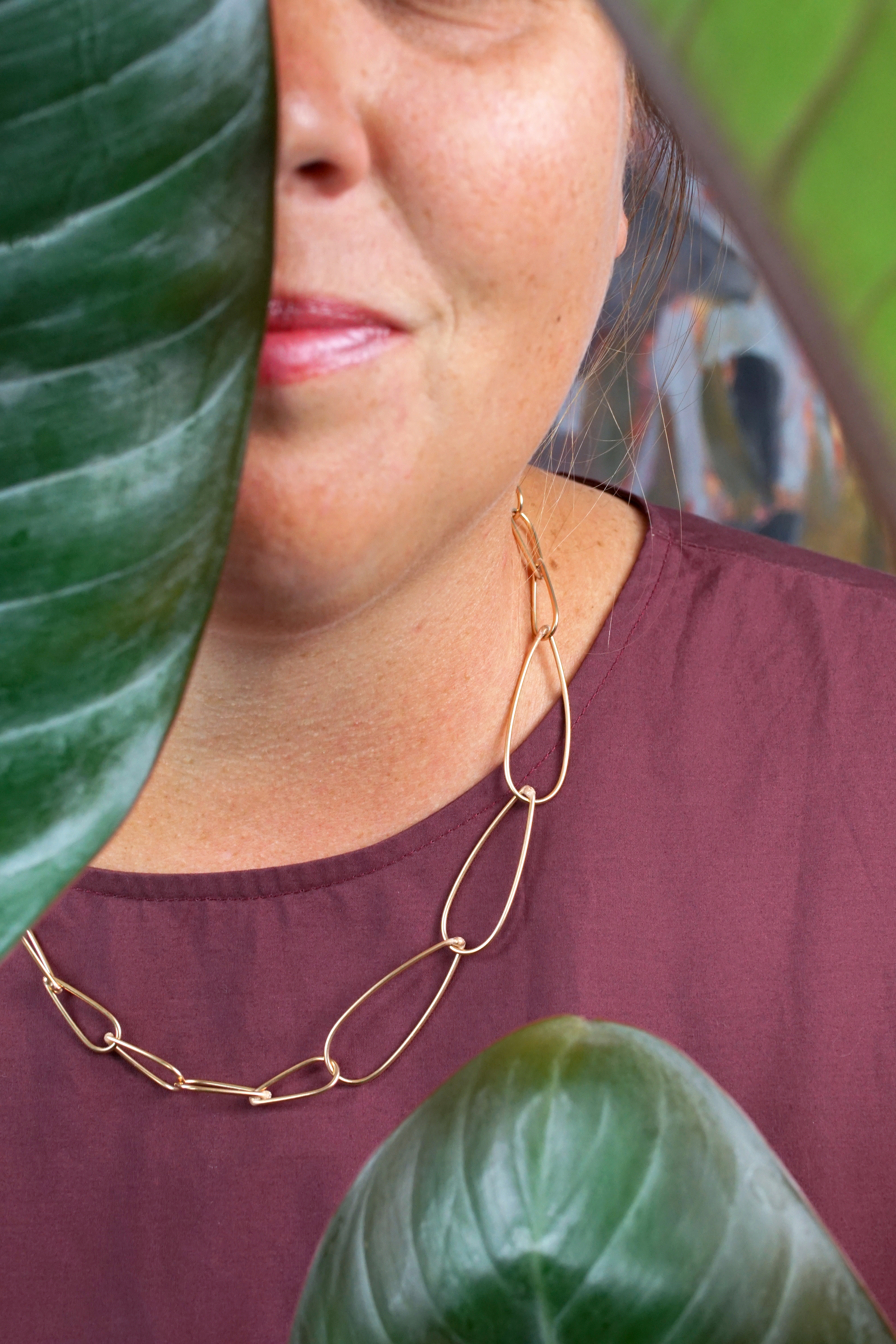 handcrafted bronze chain necklace, burgundy dress, and philodendron rojo congo