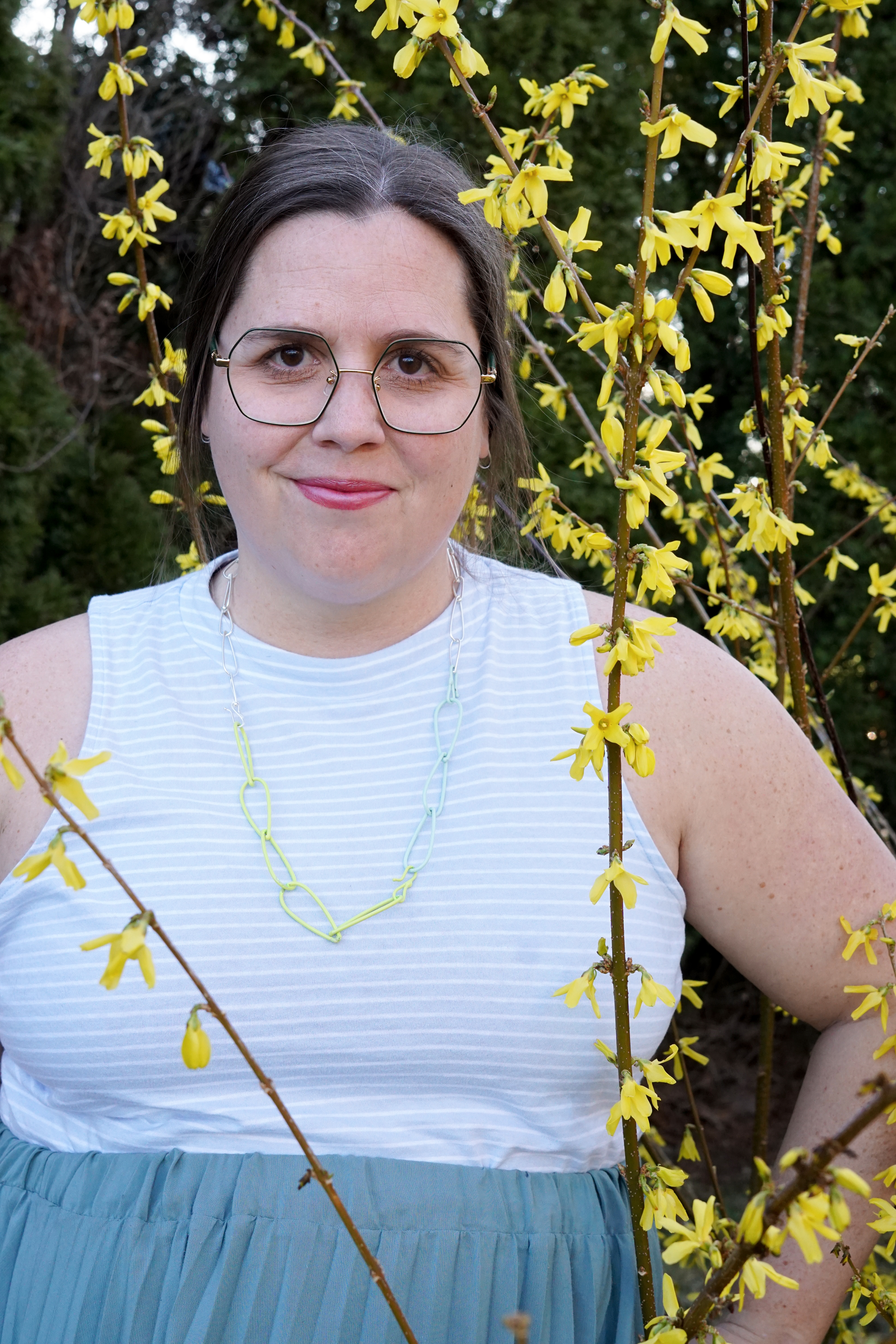 megan in neon, mint, and silver necklace with yellow flowering bush