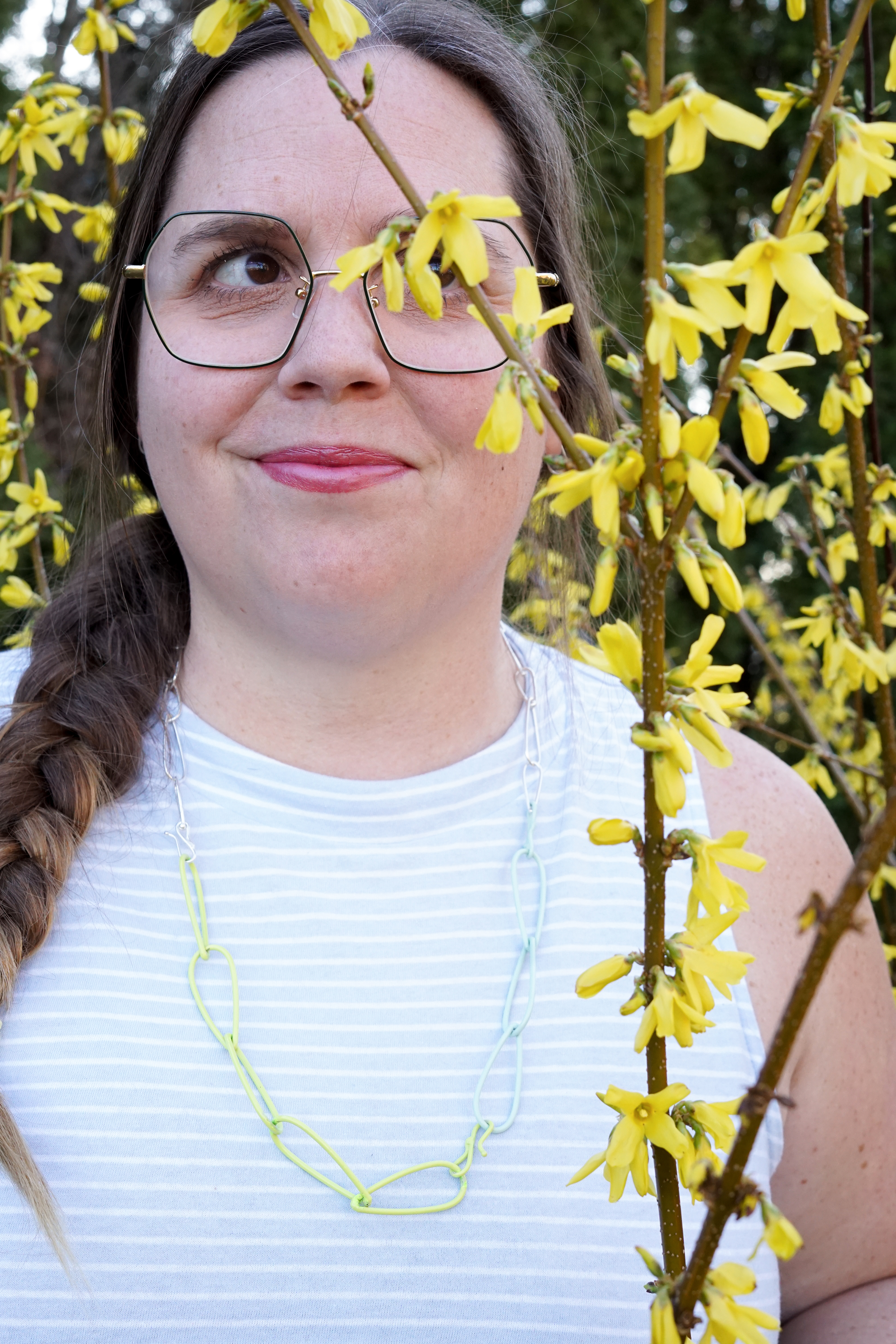 megan in neon, mint, and silver necklace with yellow flowering bush