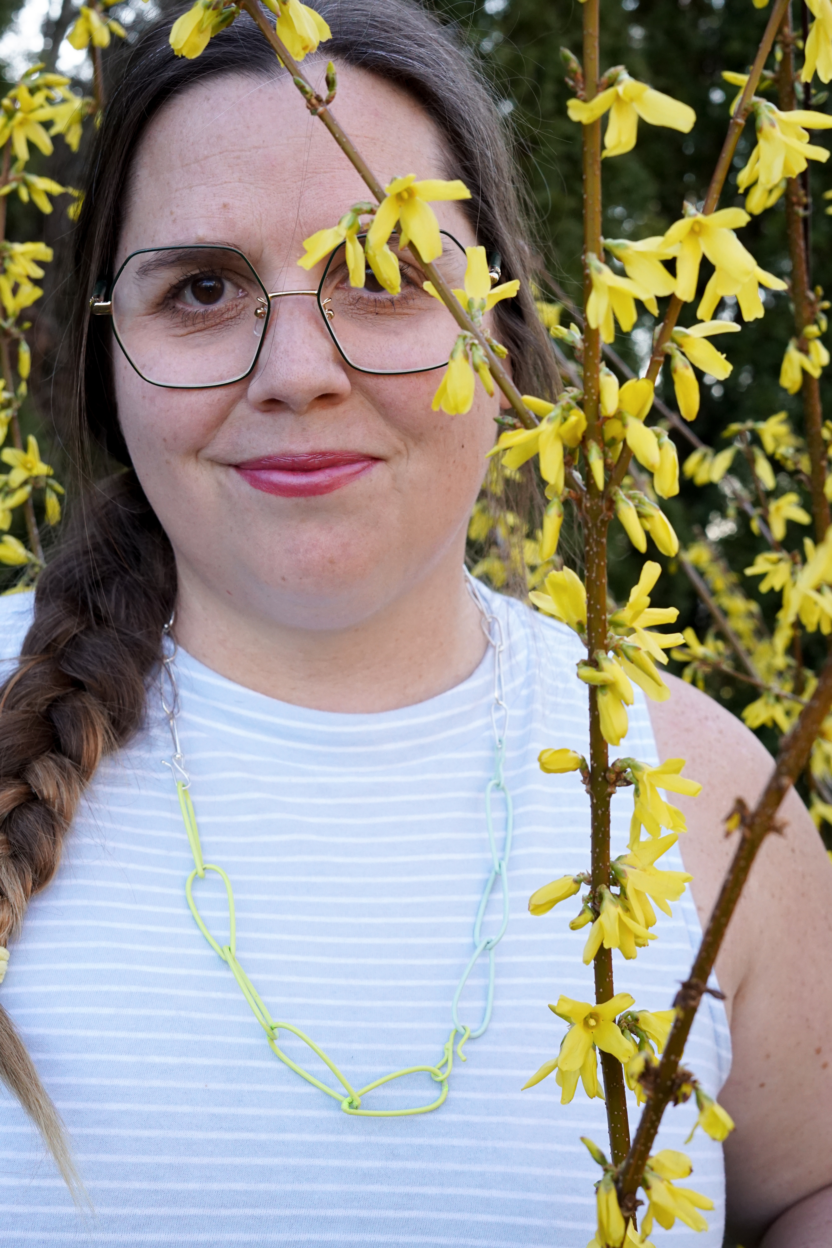 megan in neon, mint, and silver necklace with yellow flowering bush