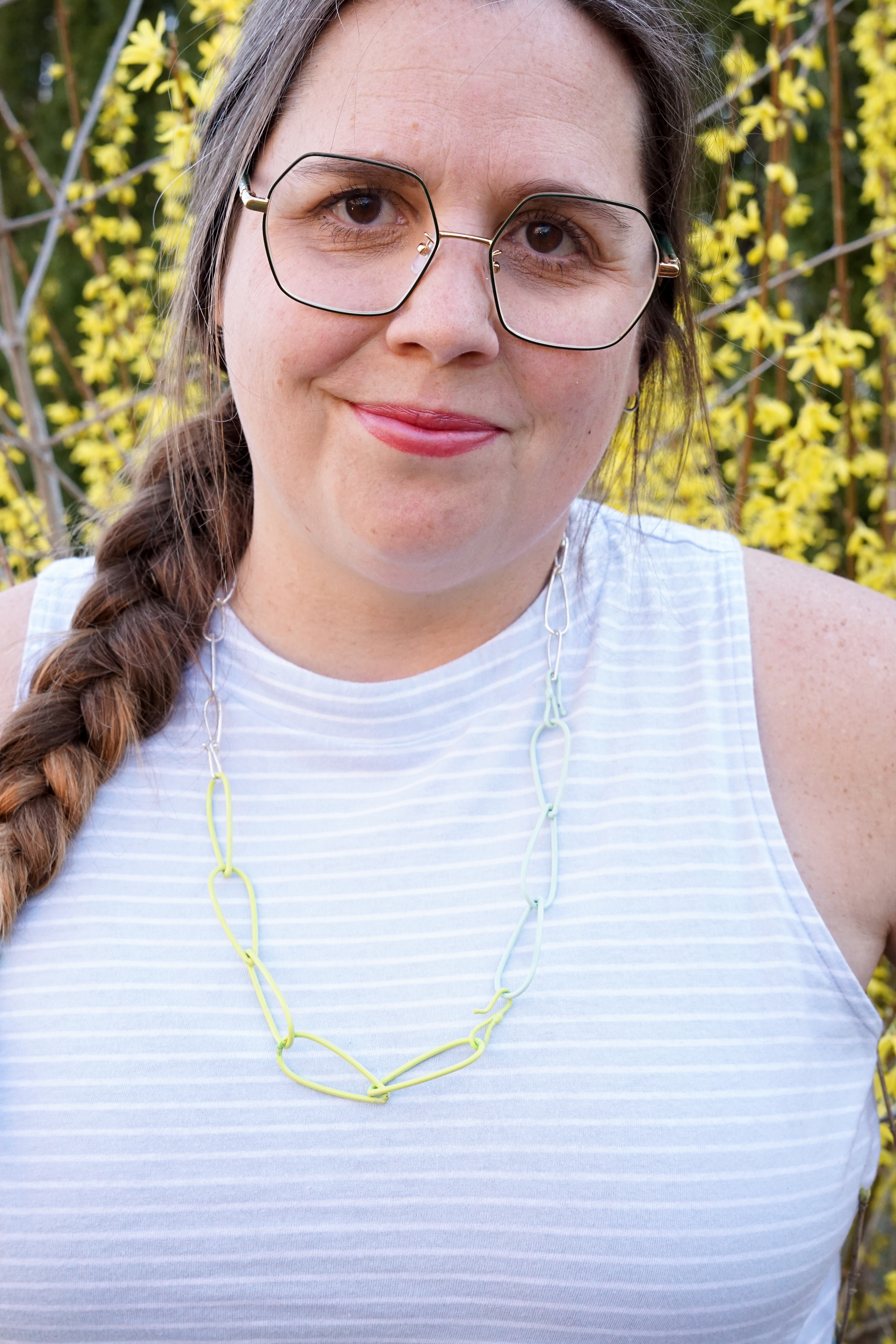 megan in neon, mint, and silver necklace with yellow flowering bush