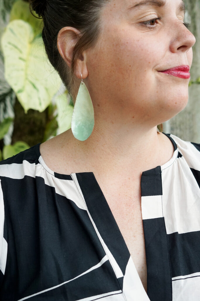light green statement earrings, plants, and black and white dress