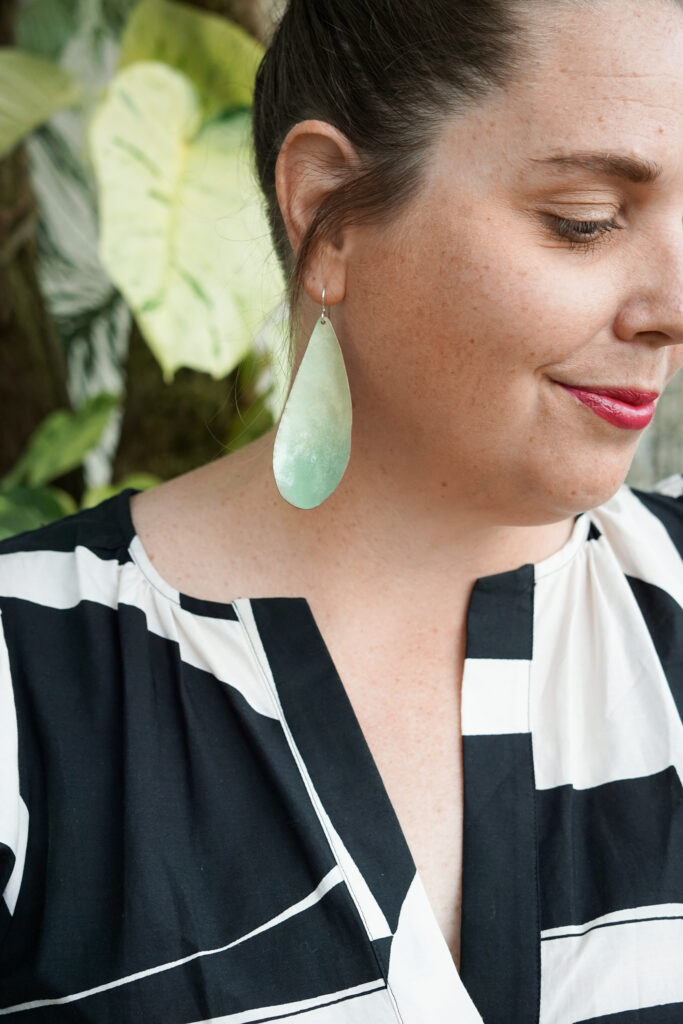 light green statement earrings, plants, and black and white dress