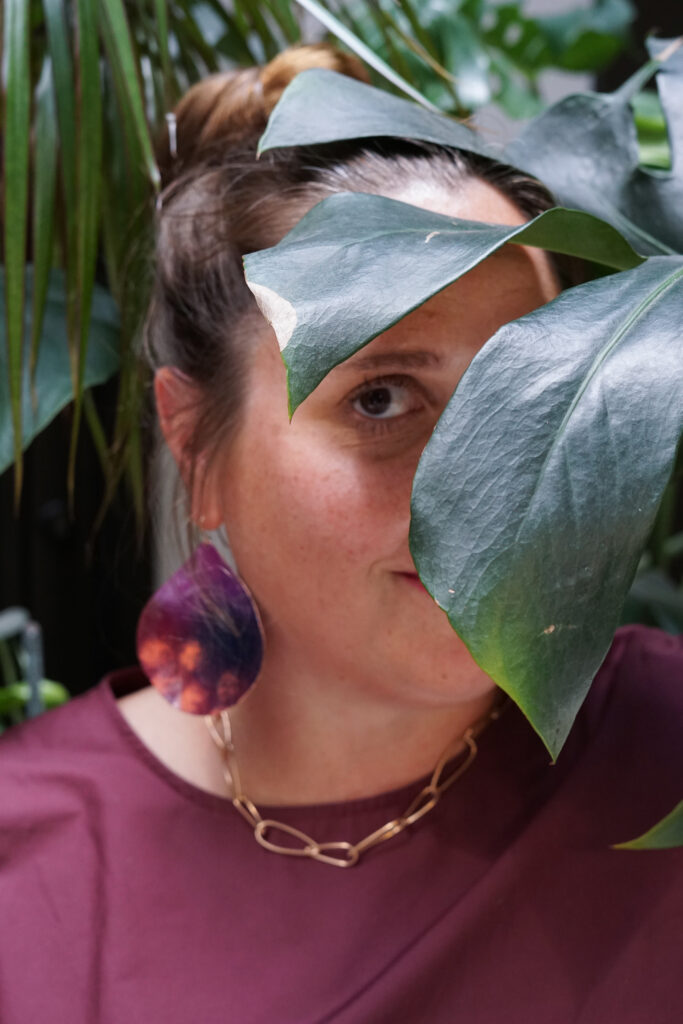 portrait with monsters plant, statement earrings, bronze chain necklace, and burgundy dress