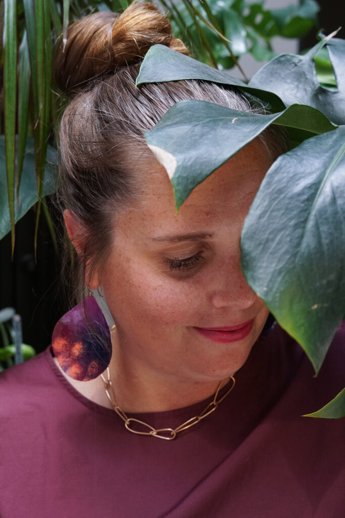 portrait with monsters plant, statement earrings, bronze chain necklace, and burgundy dress