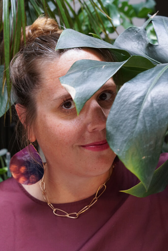 portrait with monsters plant, statement earrings, bronze chain necklace, and burgundy dress