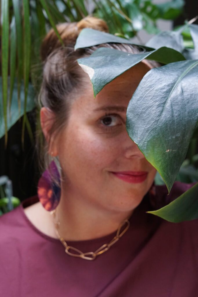 portrait with monsters plant, statement earrings, bronze chain necklace, and burgundy dress